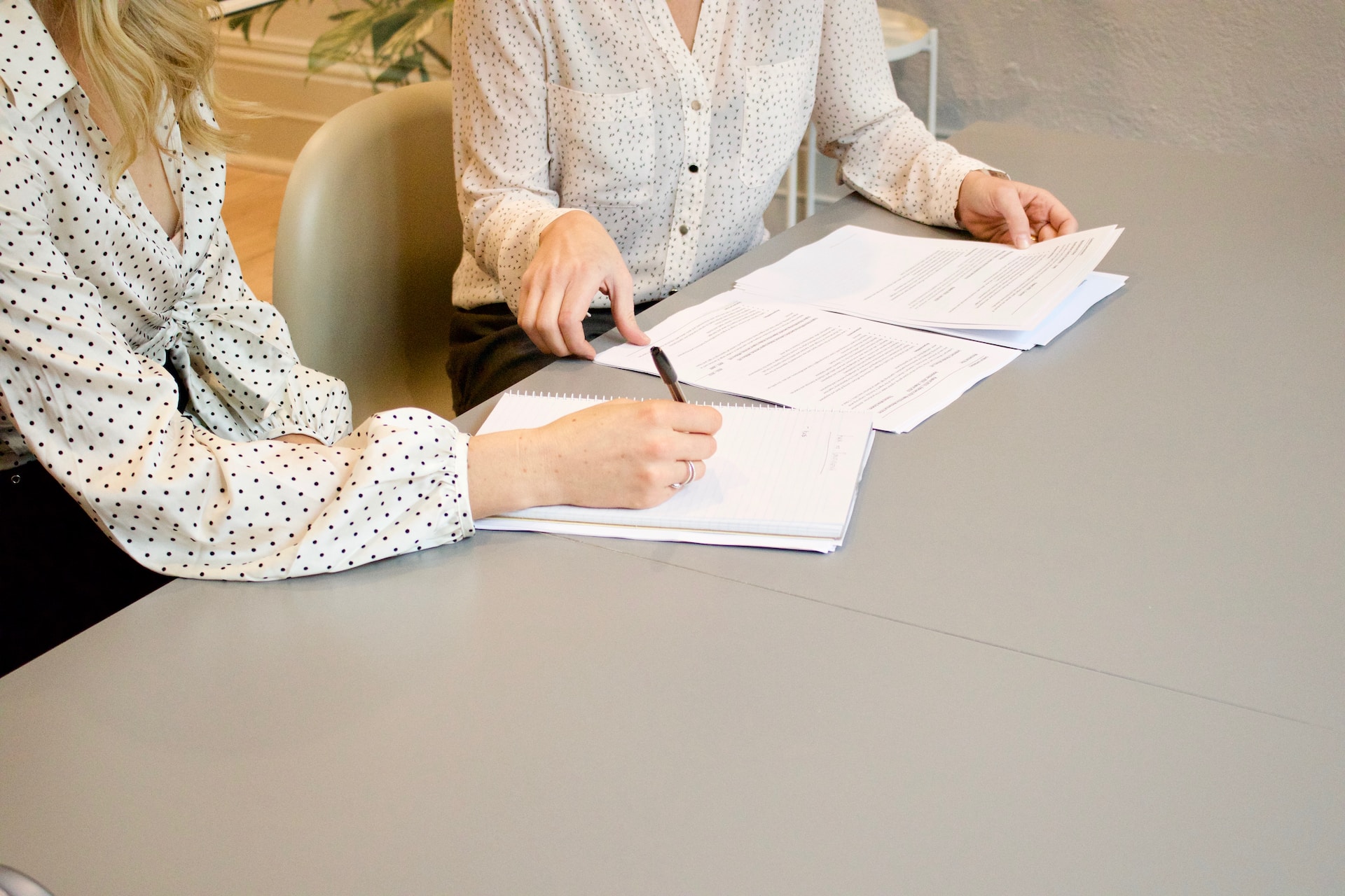 Two women at a table, one signing a form 